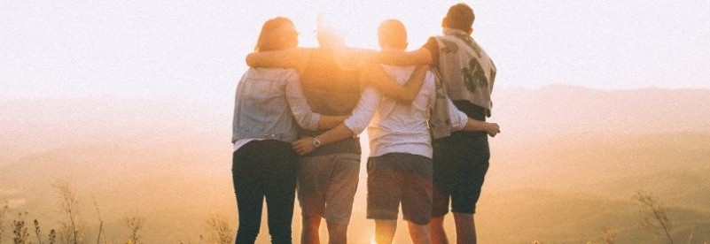 Group of people with arms around each other facing the sunset